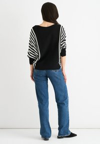 Maglione oversize a righe bianche e nere con maniche dolman, abbinato a jeans blu sbiaditi. Tessuto morbido, vestibilità casual e dettagli con polsini a coste.