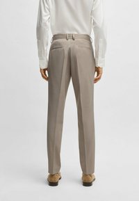 Pantaloni beige su misura con una texture liscia, dotati di frontale piatto, due tasche posteriori e vestibilità slim. Abbinati a una camicia bianca con bottoni.