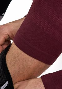 Bordowy sportowy rękaw kompresyjny z teksturowanej tkaniny. Charakteryzuje się dopasowaniem na ramieniu oraz kontrastującym czarnym elastycznym pasem na nadgarstku.