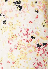 Motif floral sur tissu avec de petites fleurs jaunes, roses et rouges accompagnées d'accents noirs sur un fond crème, dans un matériau doux et texturé.