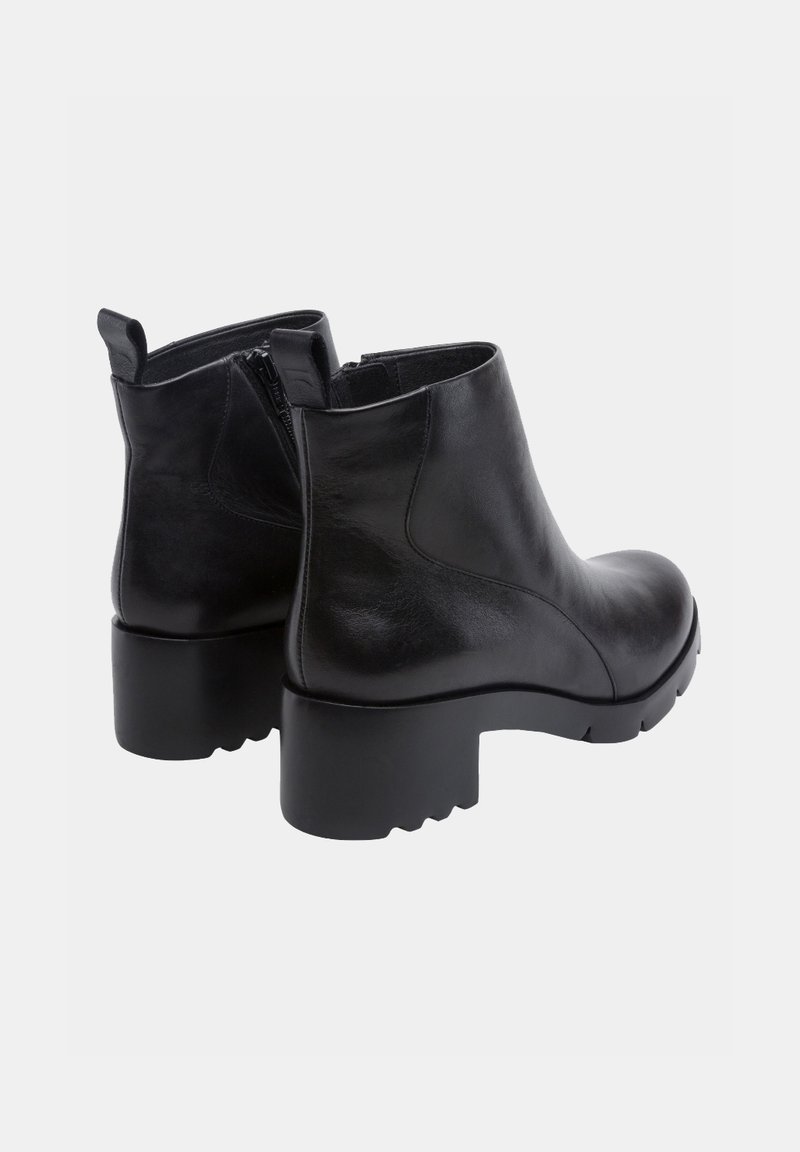 Botas de tobillo de cuero negro con un diseño elegante, cremalleras laterales y suelas de goma gruesas. Textura suave y forma de puntera redondeada.