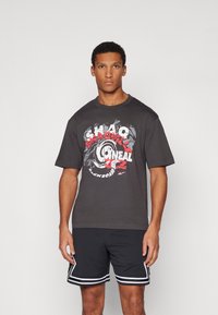 Mørkegrå t-shirt med grafisk design i rød og hvid, med fed tekst og cirkulære mønstre. Sættet er kombineret med sorte shorts og hvide accenter.