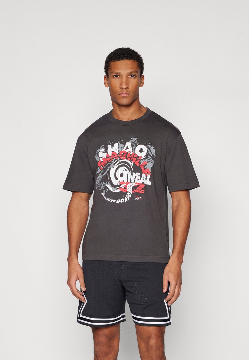 Mørkegrå t-shirt med grafisk design i rød og hvid, med fed tekst og cirkulære mønstre. Sættet er kombineret med sorte shorts og hvide accenter.