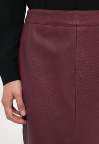 Jupe en cuir bordeaux avec une finition texturée, dotée d'une taille lisse et de subtiles coutures le long du côté.