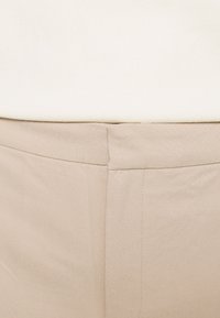 Beiga byxor med en slät yta, med flat front och rena sömmar. Kombineras med en enfärgad vit topp med en enkel design.