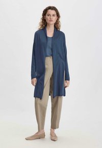 Marineblauer langer Cardigan aus weichem Stoff, mit offenem Vorderteil, lockerer Passform und langen Ärmeln, kombiniert mit beigen, gefalteten Hosen.