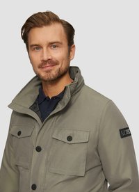 Herren grau Jacke mit hohem Kragen, zwei Fronttaschen, Knopfschluss und glatter Textur. Mit einem Markenpatch am Ärmel.