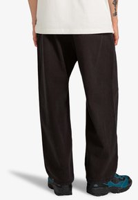 Black wide-leg pants made of denim, featuring a high waist and clean, minimalistic design. Worn with blue and black hiking shoes.