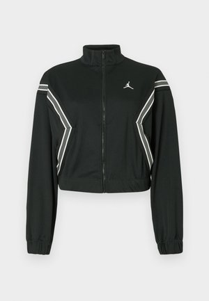 Sort cropped zip-jakke med høj krave, elastiske manchetter, hvide og grå skrå striber på ærmer og sider, samt et lille hvidt logo på brystet.