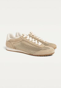 Chaussures en daim beige et mesh avec un design à lacets, présentant un bout arrondi et une semelle extérieure en caoutchouc texturée pour une meilleure adhérence.