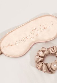 Mascherina da sogno in raso beige con accenti di strass, affiancata da un elastico in raso coordinato decorato con simili decorazioni.