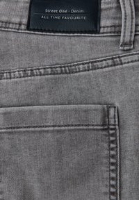 Šedá denimová látka se šitými kapsami. Obsahuje černou koženou etiketu s embosovaným nápisem "Street One - Denim" ve stříbrné barvě.