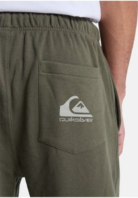 Olivgröna sweatpants med en bakficka och en vit Quiksilver-logga. Mjuk textur och elastisk midja för komfort.
