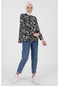 Black and white floral-patterned blouse with long sleeves, high neckline, paired with blue tapered jeans and white sneakers.