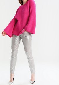 Pull rose en tricot avec manches évasées associé à un pantalon argenté métallique ajusté et des talons hauts argentés. Texture lisse et finition brillante.