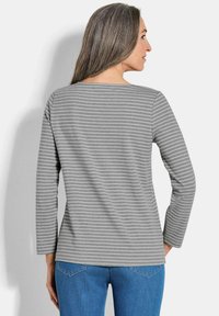 Grijze lange mouwen T-shirt met witte horizontale strepen, ronde halslijn en ontspannen pasvorm. Draagt met blauwe spijkerbroek.