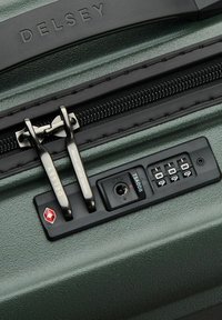 Gros plan sur la fermeture éclair d'une valise Delsey verte avec des poignées à double verrouillage et un cadenas à combinaison approuvé par la TSA réglé sur 0-0-0.