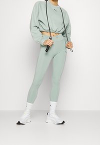 Felpa verde chiaro a maniche lunghe con orlo elastico e leggings a vita alta abbinati. Scarpe da ginnastica bianche con dettagli neri e calzini a fantasia.