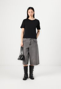 T-shirt noir à manches courtes avec un col rond, associé à un short en denim large gris. Accessoirisé avec un petit sac à main noir et des bottes hautes aux genoux.