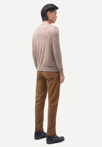 Hellbrauner Pullover mit Rundhalsausschnitt aus weichem Stoff, kombiniert mit dunkelbraunen Cordhosen und schwarzen Stiefeletten. Silhouette des Modells von hinten sichtbar.