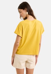 T-shirt en coton jaune à manches courtes, avec une coupe décontractée et un col rond, associé à un short beige.