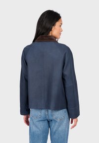 Námořnická modrá kožená bunda s hnědým manšestrovým límcem, zkrácený střih a raglánové rukávy, v kombinaci s světle modrými džíny.