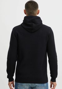 Marineblauwe hoodie gezien vanuit de achterkant. Kenmerkt zich door een ribbelzoom en manchetten, zachte textuur en een minimalistisch ontwerp.