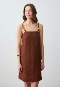 Braunes Leinenkleid mit dünnen Trägern, das dekorative Perlen in verschiedenen Farben an den Schultern aufweist. Schlicht, lockere Passform und knielang.
