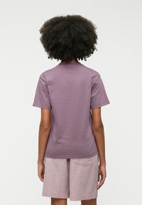 T-shirt κοντομάνικο, με στρογγυλή λαιμόκοψη σε ήπιο μωβ, κατασκευασμένο από μαλακό ύφασμα. Φοριέται με ανοιχτό ροζ σορτσάκι με υφασμάτινο μοτίβο.