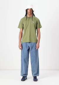 Olive green cotton t-shirt, short sleeves, crew neck. Loose-fitting light blue denim jeans. White bucket hat. Navy sneakers with white stripes.