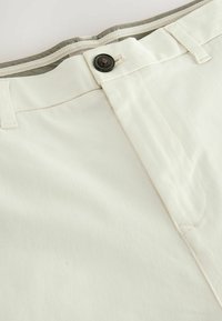 Pantalones de algodón blancos con una cintura gris, cierre de botón y sutiles detalles de costura. Textura suave con elementos de diseño mínimos.