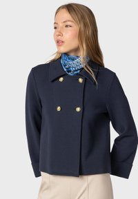 Navy double-breasted jacket with gold buttons, featuring a lapel collar and casual fit. Accompanied by a blue patterned scarf.