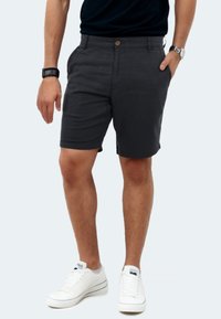 Dark gray shorts made of lightweight fabric, featuring two side pockets, a front button closure, and a tailored fit. Worn with white sneakers.