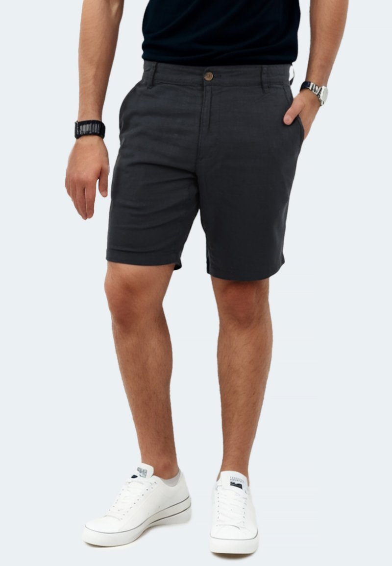 Dark gray shorts made of lightweight fabric, featuring two side pockets, a front button closure, and a tailored fit. Worn with white sneakers.