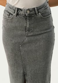 Falda lápiz de denim gris con una abertura frontal, cintura alta, bolsillos y detalles de botones metálicos. La tela tiene una ligera textura y un acabado deslavado.