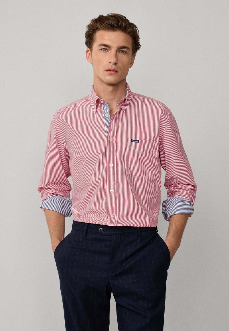 Chemise à rayures rouges et blanches avec un col d'accent bleu, associée à un pantalon bleu marine à rayures. Comprend une poche poitrine et des manches retroussées.