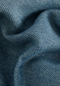 Denim tkanina u različitim nijansama plave boje s tkanim uzorkom, s mekim naborima i suptilnim ribljim kostima.