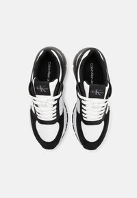 Baskets noir et blanc avec une tige synthétique lisse, dotées d'une semelle épaisse, de lacets et d'un logo sur la languette. Accents texturés le long du design.