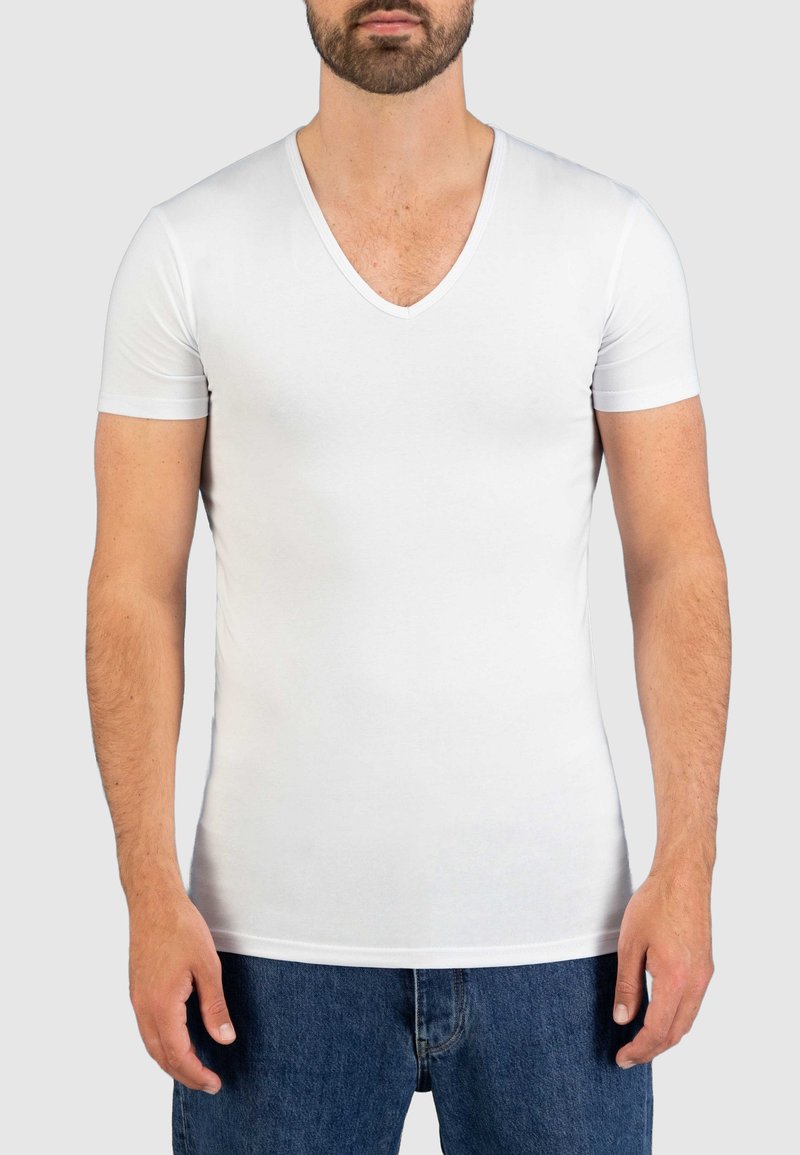 Witte T-shirt met korte mouwen en V-hals, gemaakt van rekbaar materiaal, met een aansluitend ontwerp dat het lichaam accentueert, gecombineerd met blauwe denim shorts.