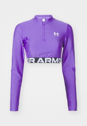 Top corto de manga larga púrpura con media cremallera, que presenta un diseño ajustado y una banda negra "Under Armour" a lo largo del dobladillo. Fabricado con tejido suave.