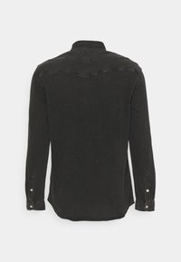 Camicia di jeans nera a maniche lunghe con polsini a bottoni, con yoke in stile western sul retro, mostrata da dietro su sfondo bianco semplice.