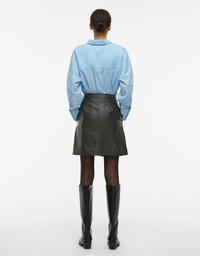 Blåstripet skjorte med ledig passform, svart skinnminiskjørt og knelang svarte støvler, med glatte teksturer og skreddersydde detaljer.