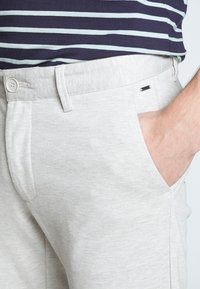 Light grey trousers made of soft fabric, featuring a button closure, side pockets, and a small black accent near the waistband.