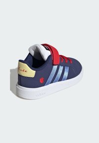 Blå sneakers med röda detaljer, vit sula och kardborreband. Har tre ljusblå ränder och broderad äppellogo på hälen.