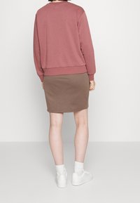 Světle růžová mikina s žebrovanými manžetami, doplněná hnědými sukněmi po kolena. Bílá sneakers a bílé ponožky do půlky lýtek dokončují outfit.