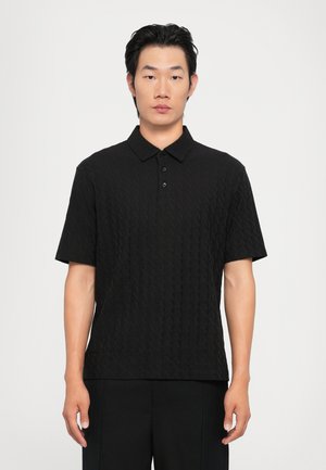 Svart kortermet polo-skjorte med et teksturert diamantmønster, med krage og tre knapper, kombinert med mørke bukser.