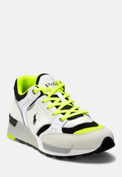 Sneaker med ett vitt och svart överdel, neongula accenter, nätpaneler och en tjock grå mellansula. Inkluderar gröna snörningar och logodetalj.