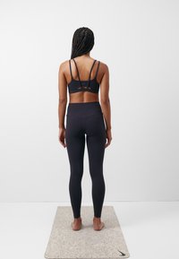 Svart sportsbh med flere tynne stropper og matchende høyt liv leggings. Glatt, elastisk stoff, vist mot en lys bakgrunn.