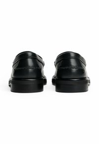 Zapatos de cuero negro tipo mocasín con punta redondeada, que cuentan con detalles de costura y suela de estilo madera. Textura suave con poca ornamentación.