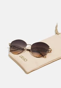 Gold metal sunglasses with gradient brown lenses. Features chain accents on the arms. Includes a beige soft case with "LIU JO" branding.